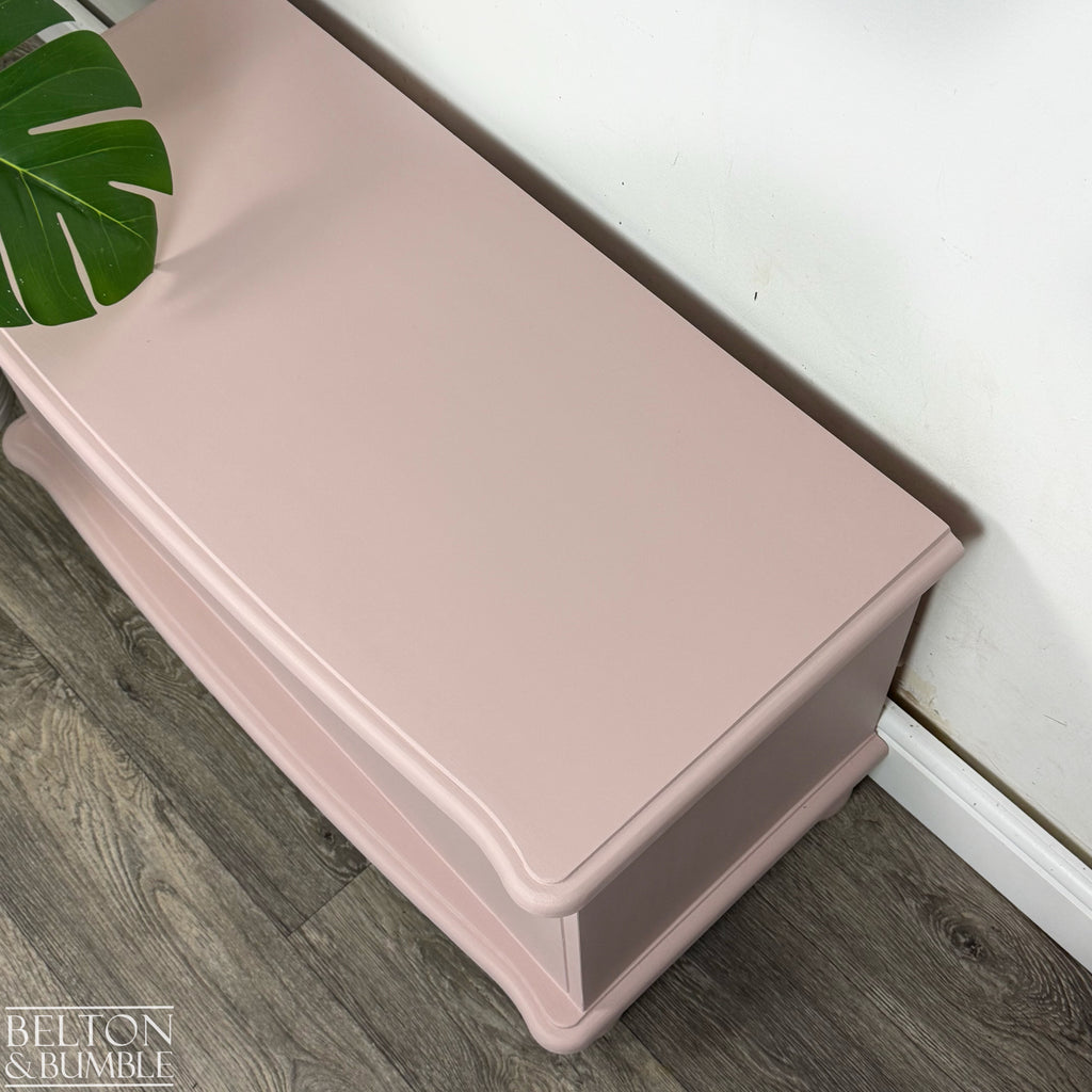 Side angle of blush pink blanket chest showing soft curved lid and neat ball feet.