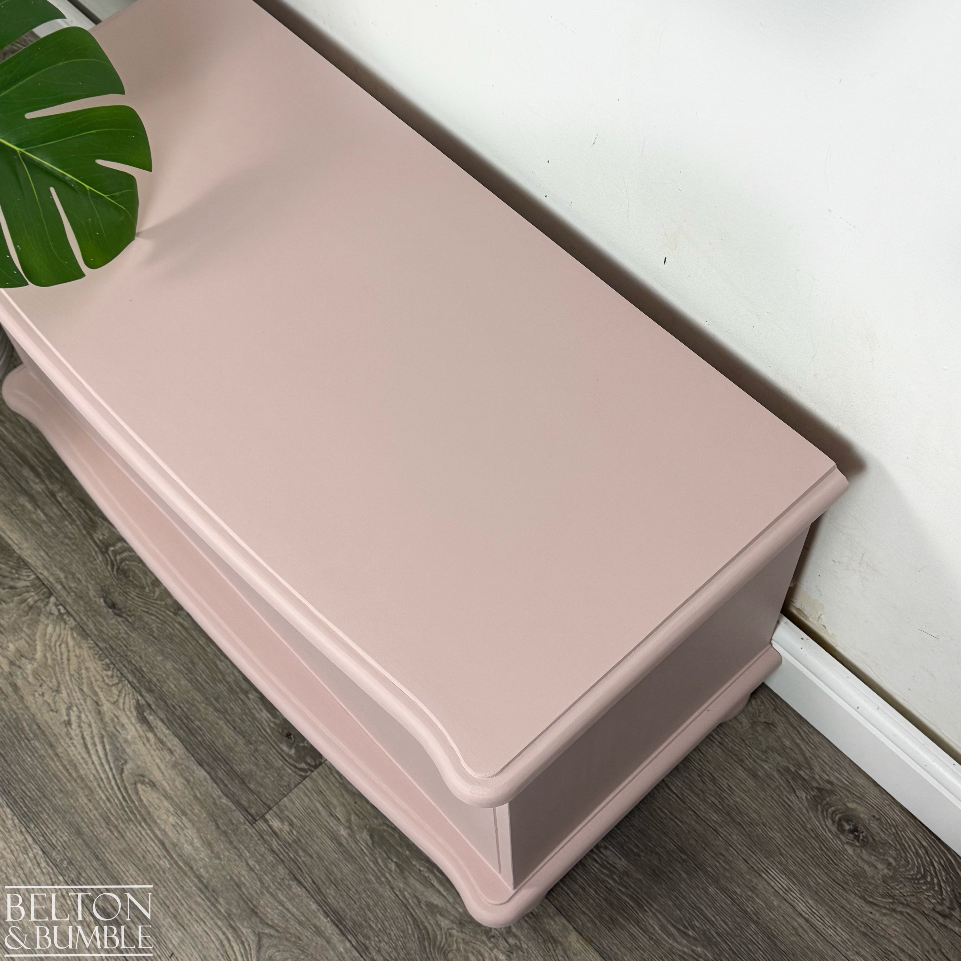 Side angle of blush pink blanket chest showing soft curved lid and neat ball feet.