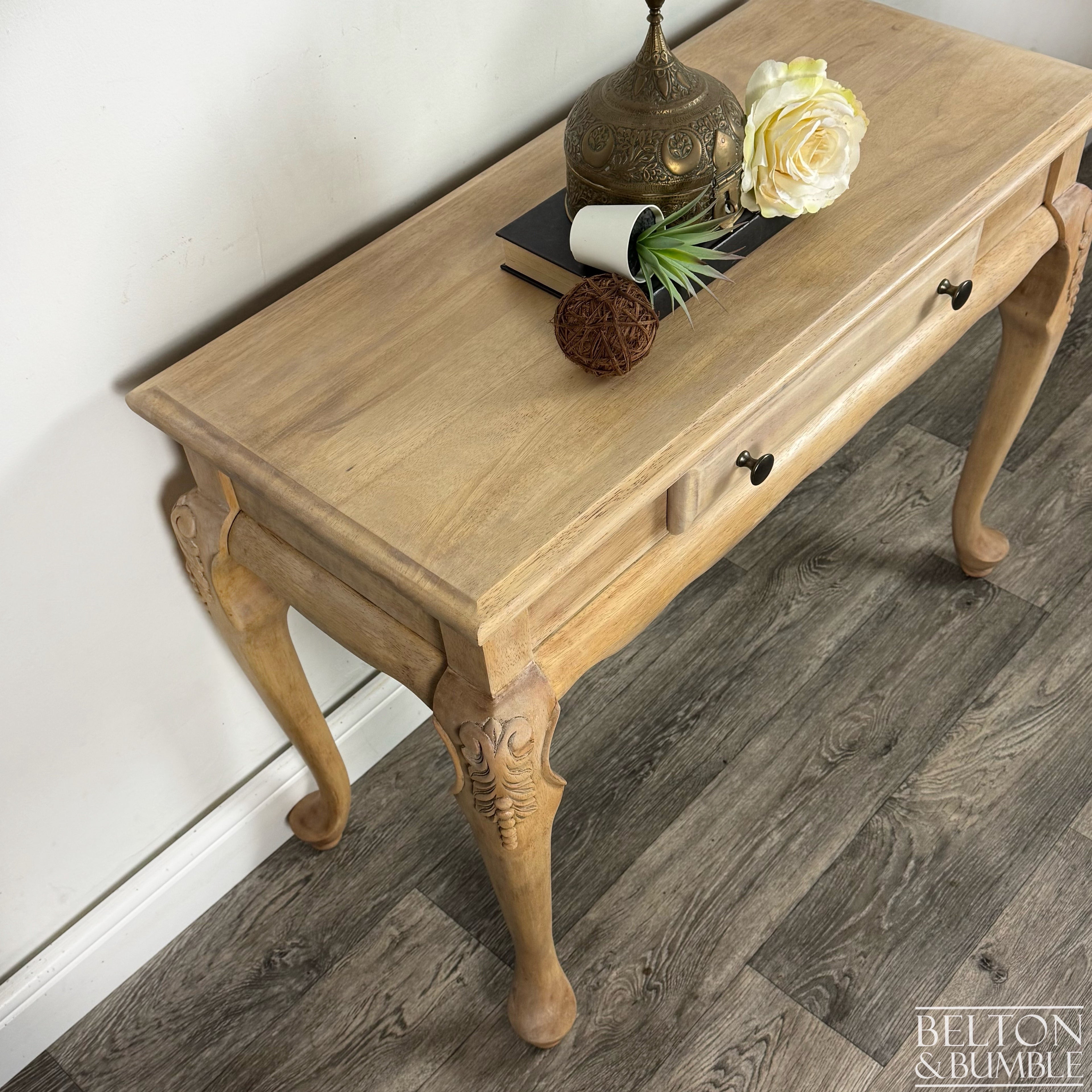 Side angle of light wood console table showing elegant carved legs, scalloped apron, and smooth natural finish.