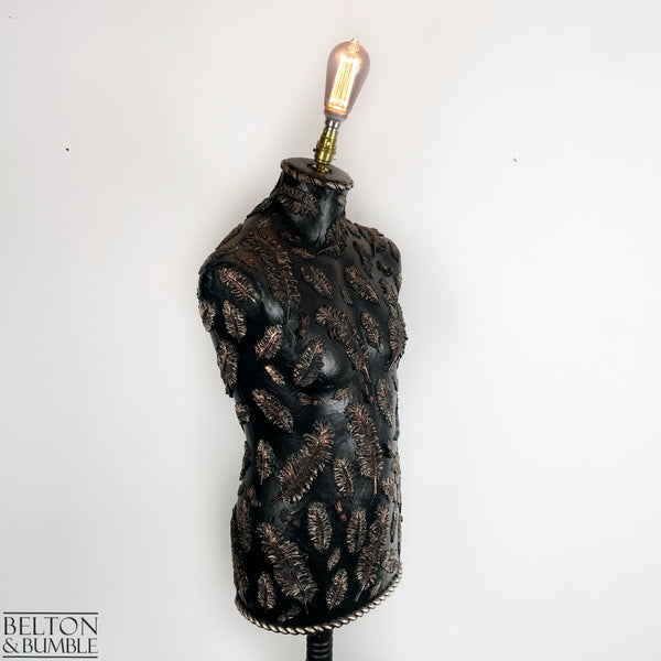 Black and Copper Feather Mannequin Lamp with Black Wooden Stand - A mannequin lamp with a black and copper feather design, mounted on a black wooden stand with a visible bulb.