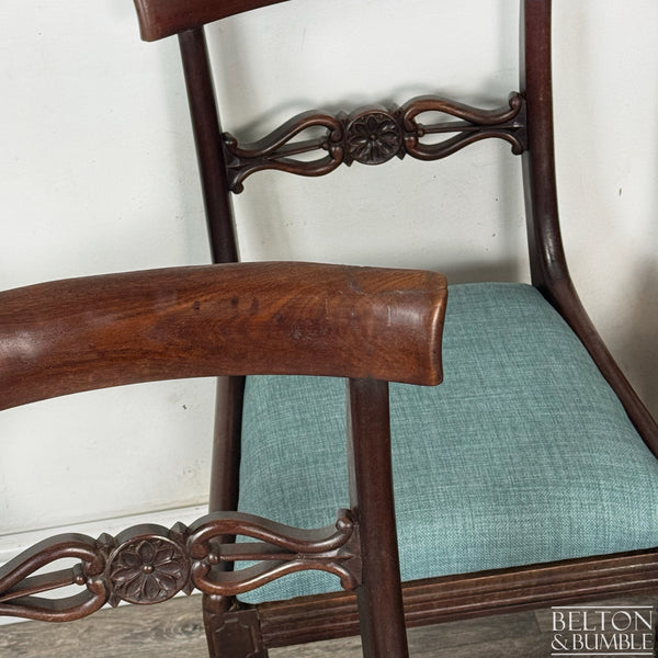 Close-up of a mahogany dining chair showing the curved top rail, floral carved back splat, and teal upholstered seat, highlighting the wood grain and craftsmanship of the design.