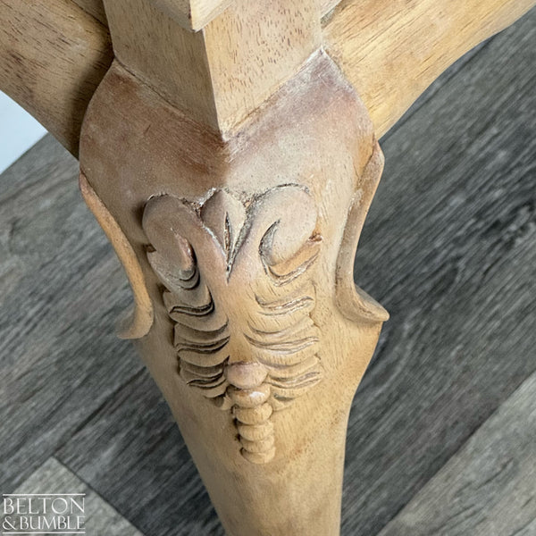 Detailed view of decorative carving on the table leg showing intricate leaf pattern in natural wood grain.