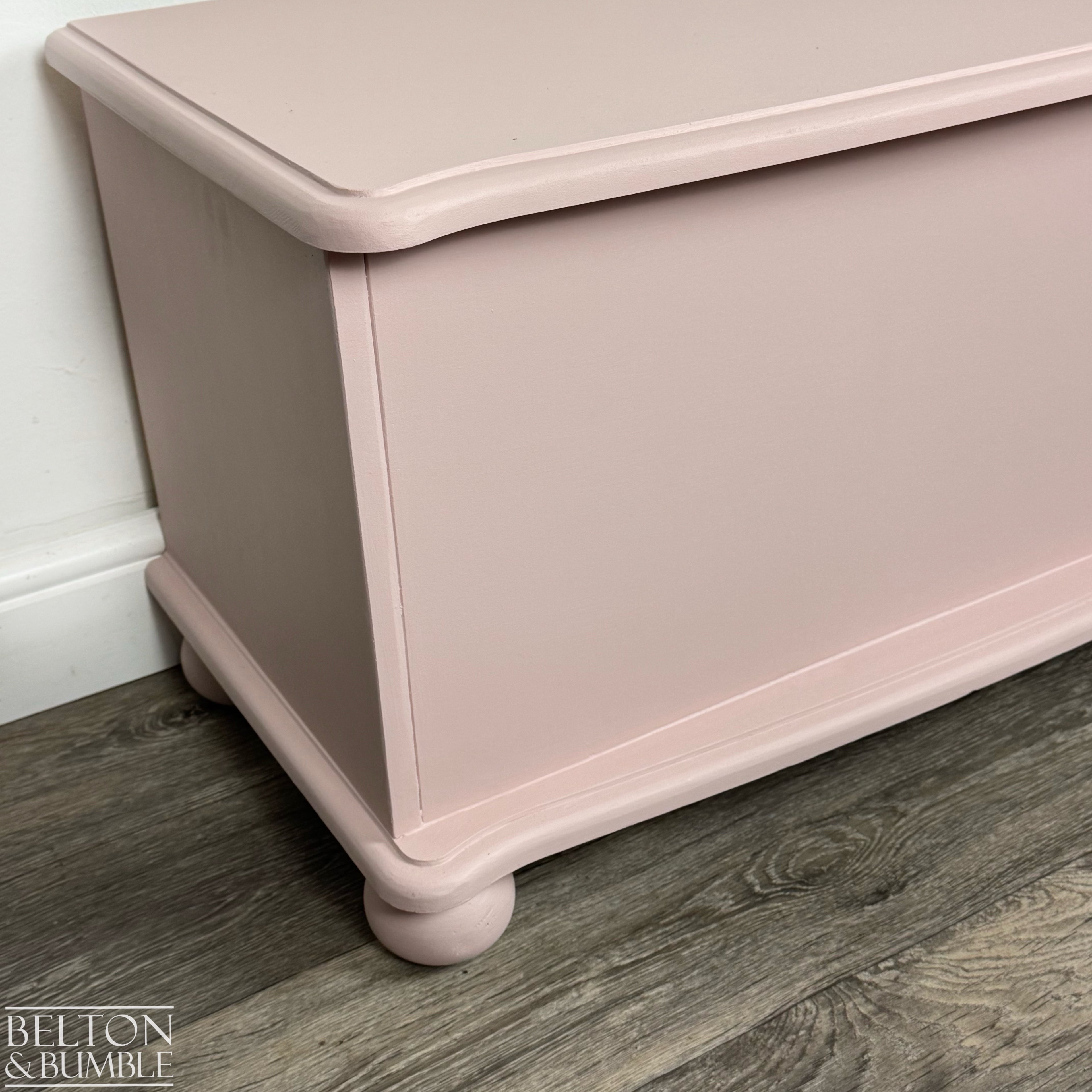 Close-up of the corner of the pink storage chest showing smooth painted finish and rounded edge detail.
