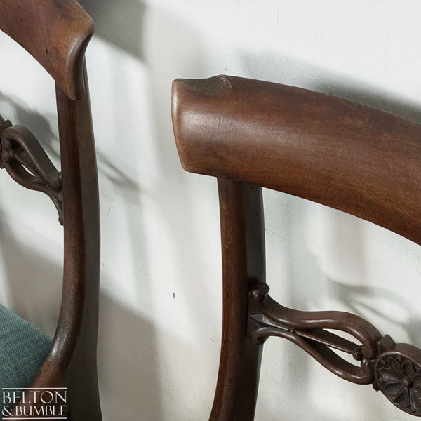 Close-up view of a mahogany dining chair showing the curved top rail, carved back detailing, and rich wood grain, with part of a teal upholstered seat visible below.