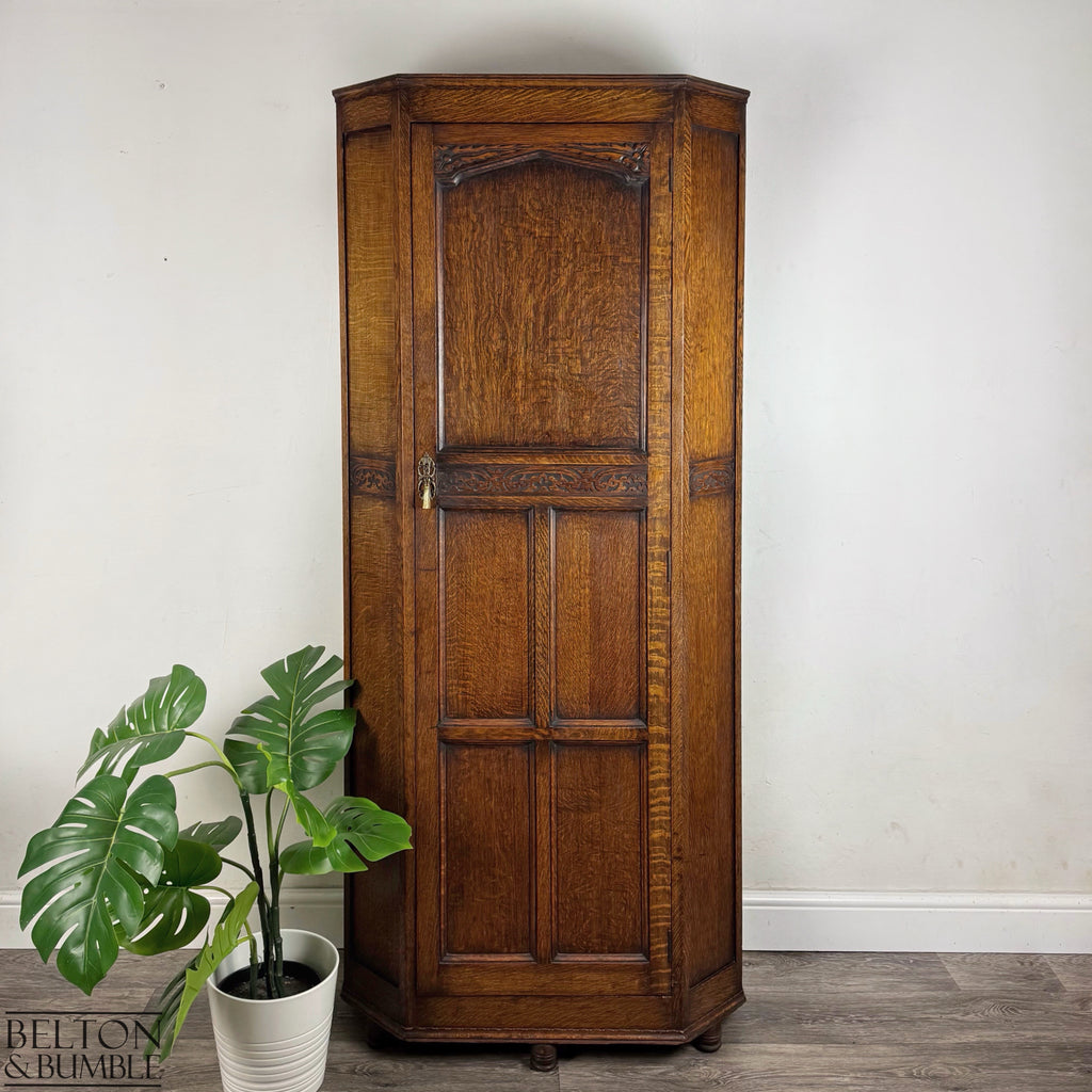 Front view of an Edwardian solid oak single-door wardrobe with carved detailing and bun feet.