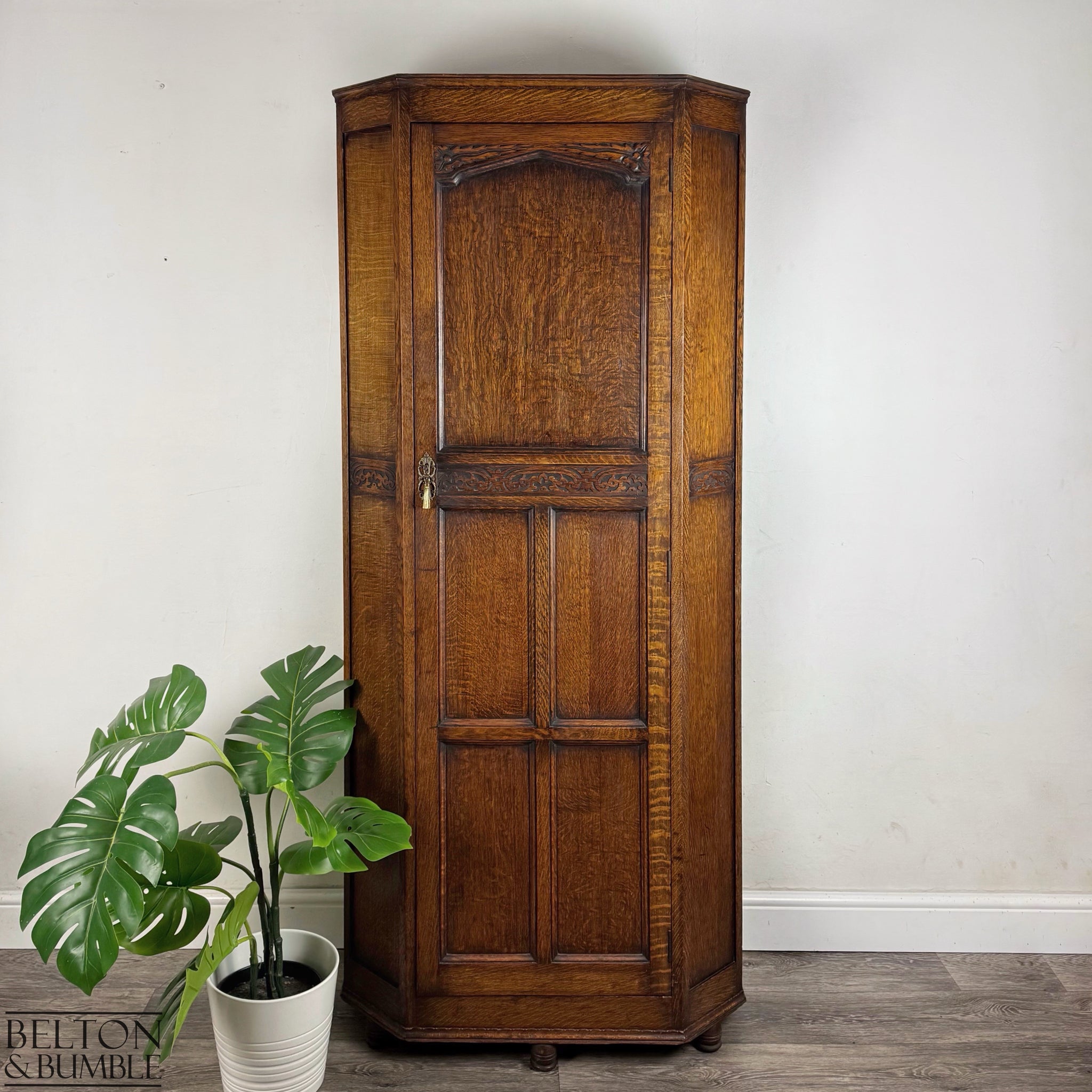 Front view of an Edwardian solid oak single-door wardrobe with carved detailing and bun feet.