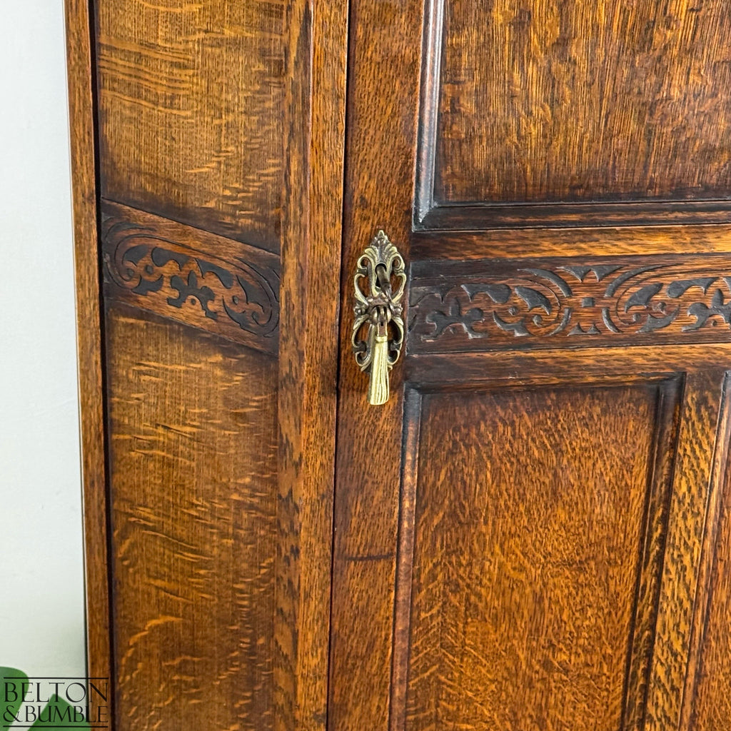 Close-up of the carved brass escutcheon, decorative panelling, and warm oak grain on the Edwardian wardrobe.