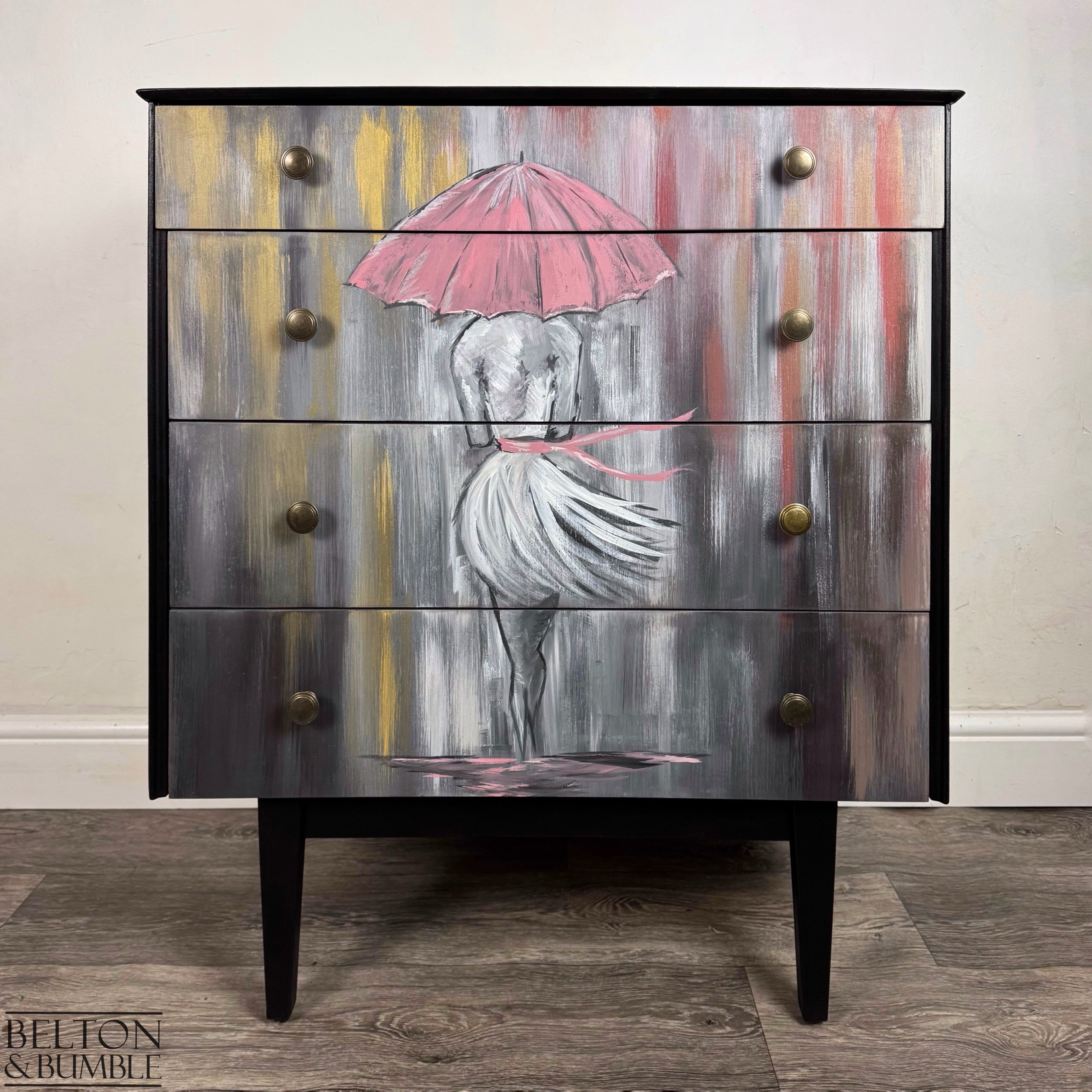 Hand-painted black drawers featuring pink umbrella artwork, brass knobs, and mid century modern legs.