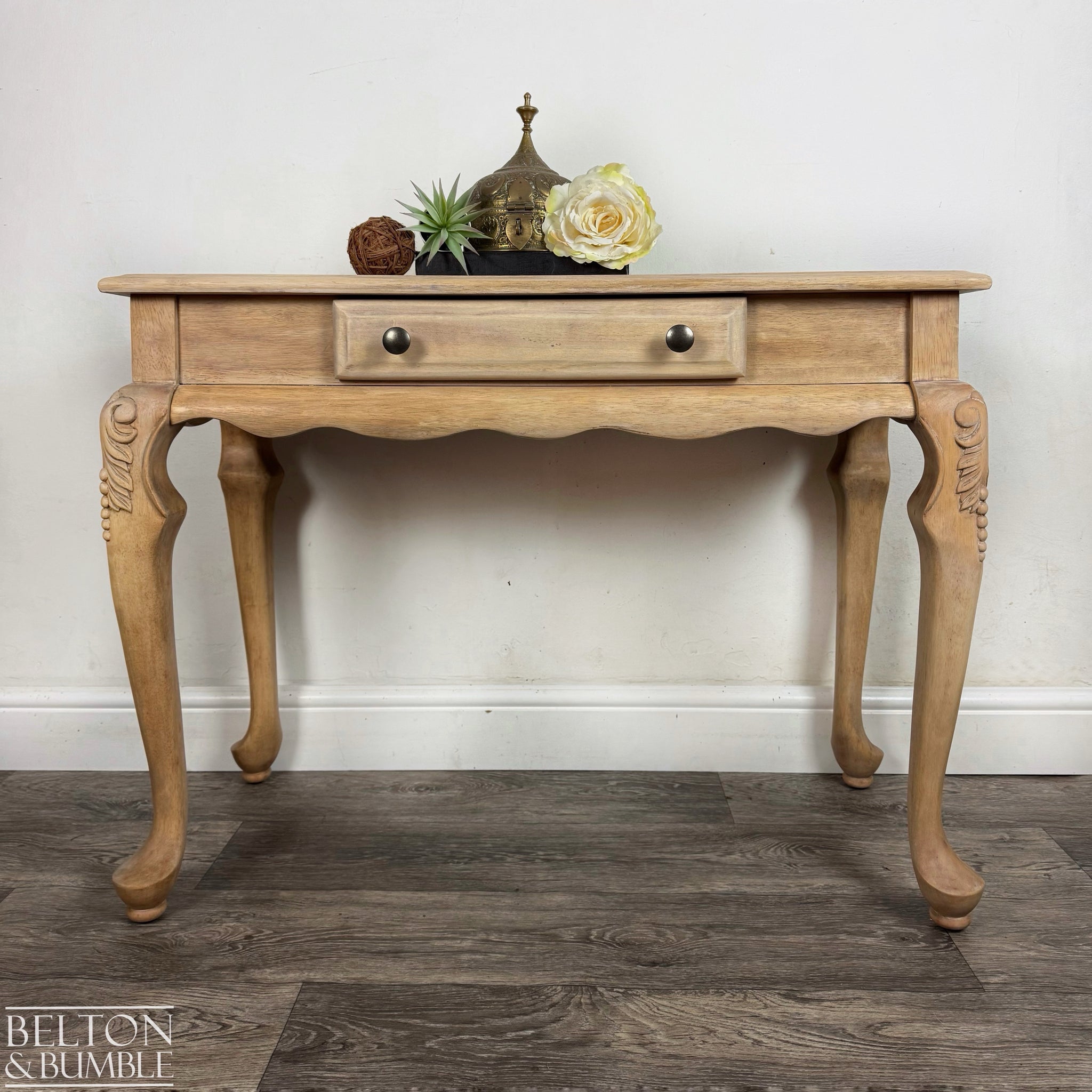 Natural light wood console table with carved legs and single drawer, styled with neutral decorative accents.