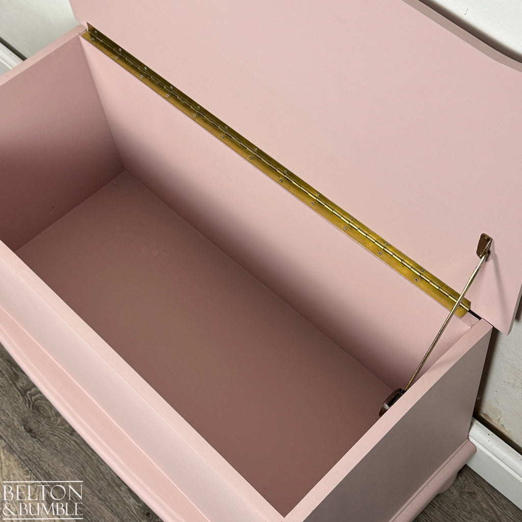 Close-up of open blush pink blanket chest highlighting brass hinge and internal storage space.