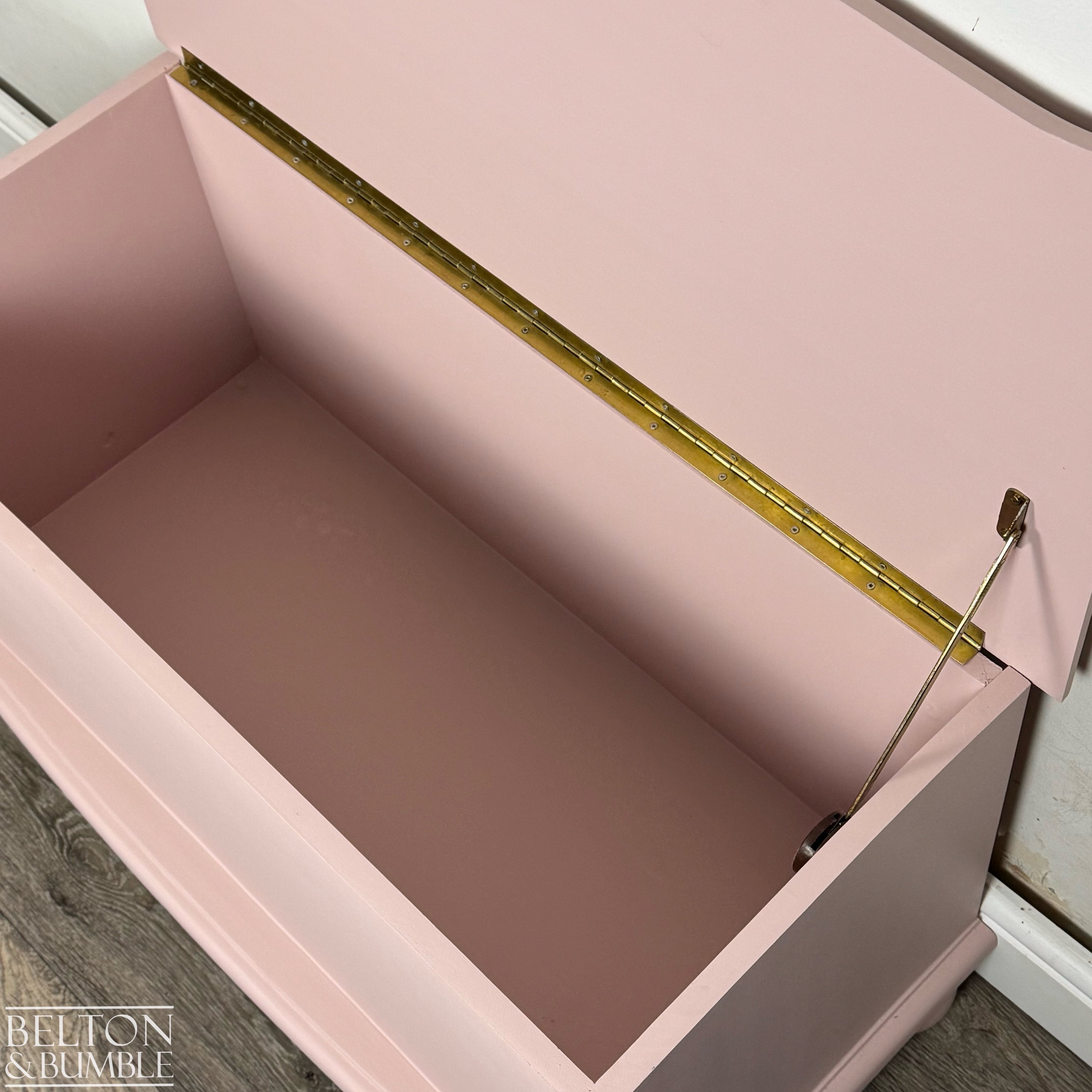 Close-up of open blush pink blanket chest highlighting brass hinge and internal storage space.
