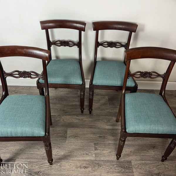 Four mahogany dining chairs with carved back details and teal upholstered seats arranged in a semi-circle on wood flooring against a plain light wall, showcasing their elegant craftsmanship and classic design.