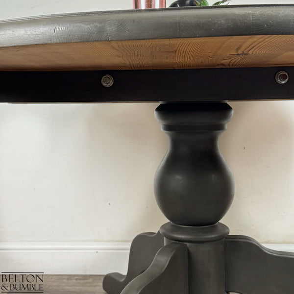 Side view of the circular pedestal dining table with natural pine top and dark grey base.