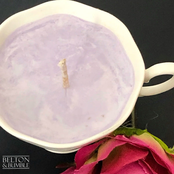 Soy Wax Petite Teacup with Black Cherry Scent - Overhead view of a petite soy wax teacup candle with a pale lilac colour and natural wick, surrounded by a pink rose accent.