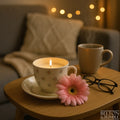 Soy Wax Vintage Teacup and Saucer Candle with Vanilla Scent - Glowing vanilla-scented soy candle in a vintage teacup and saucer, styled with a pink flower in a cosy living room setting.