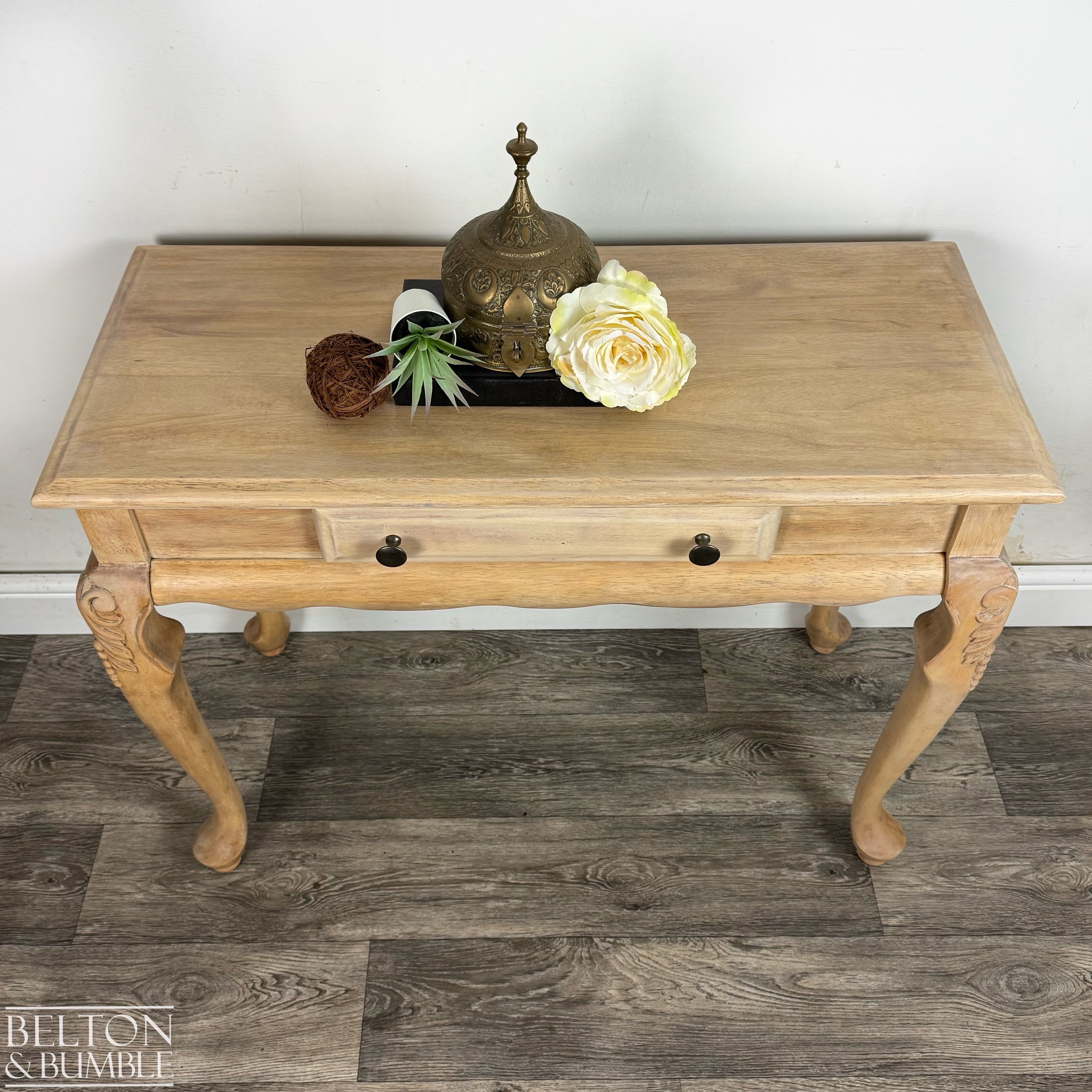 Overhead view of light wood console table featuring drawer and styled décor including a brass ornament and flower.