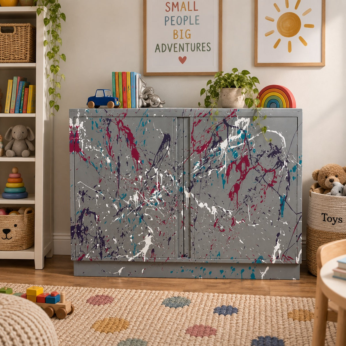 A gray metal storage cabinet with a colorful splatter paint pattern, styled in a children's room with toys, a bookshelf, and framed wall art.