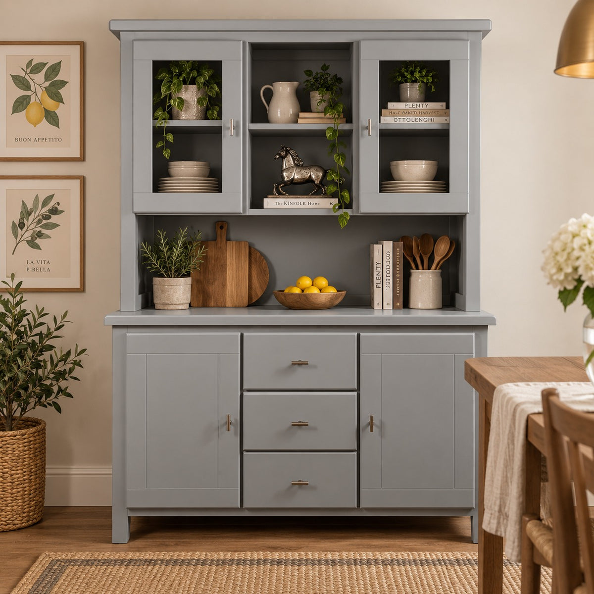 A tall gray hutch cabinet with glass-front upper cabinets, open shelves, drawers, and lower cabinet doors, styled in a dining room with plants, books, bowls, and lemons.